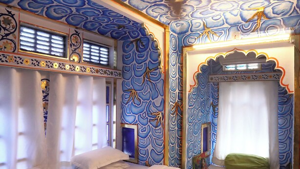 Una habitación con cama, ventana con cortinas y pared con diseño azul.