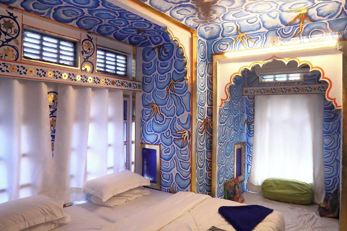 Una habitación con cama, ventana con cortinas y pared con diseño azul.