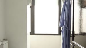 Un baño con inodoro, una ventana y una bata azul colgada en un perchero.