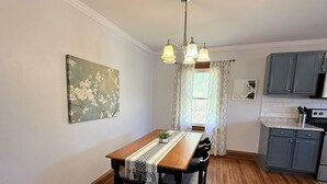Un comedor con una mesa de madera, sillas, una araña y una cocina al fondo.