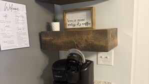 Una cocina con una cafetera sobre una encimera de granito, repisas de madera arriba y un cartel que dice 'menos es más a menos que sea café'.