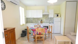 A compact kitchen with white cabinets, a microwave, and a stove. There is a dining table with chairs and a small white table. - GITE MURIER WITH POOL AND RIVER (Berrias-et-Casteljau)