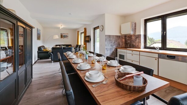 Una cucina moderna con un lungo tavolo da pranzo apparecchiato, un divano sullo sfondo e vista sull'esterno.
