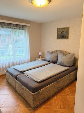A bedroom with a bed, a nightstand, a lamp, a window with curtains, and a painting on the wall. - Your forest time-out by the lake: Digital detox 1-4 pers. (Neu Poserin)