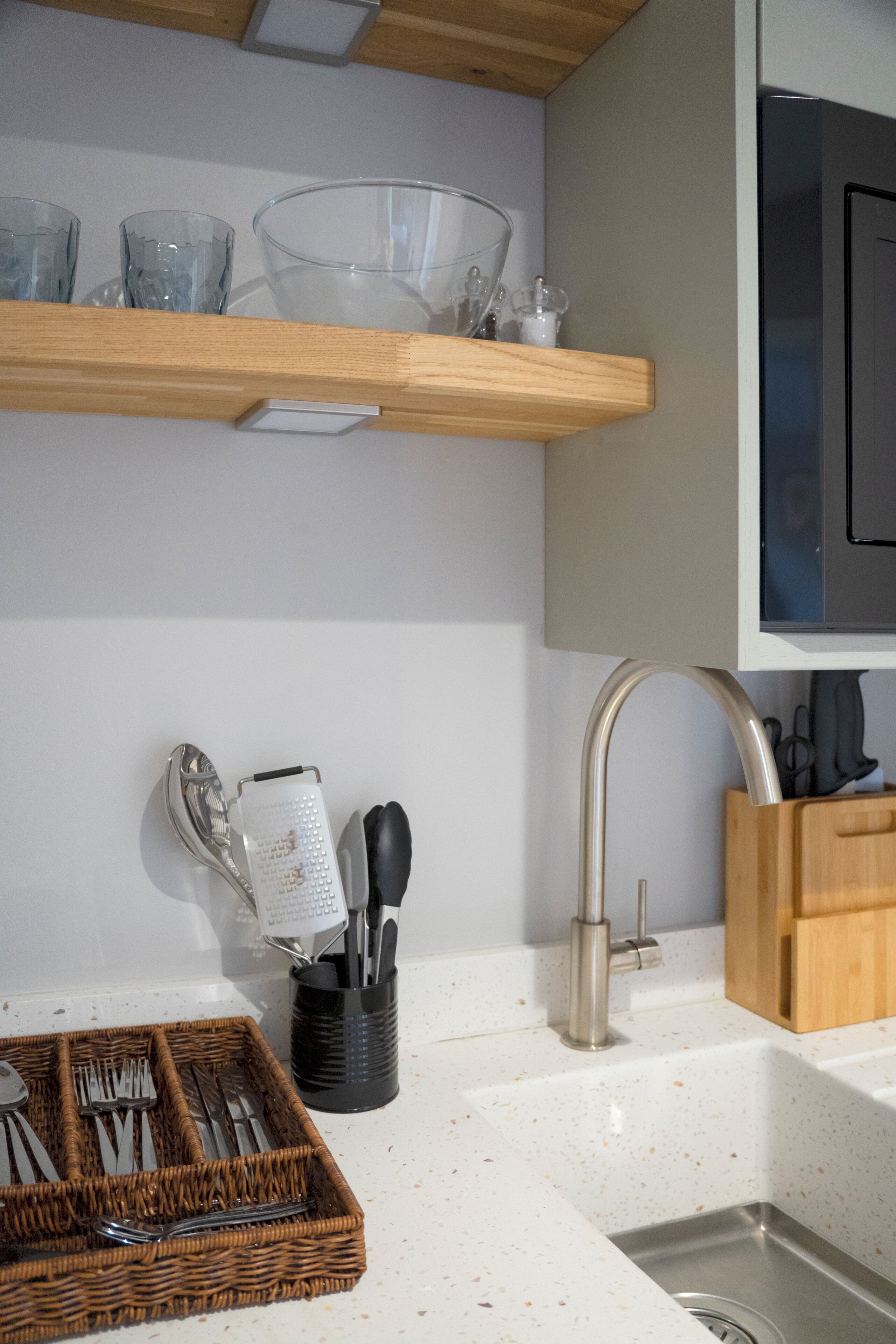Een keuken met een RVS spoelbak, een houten aanrechtblad, een mand met keukengerei en een messenblok.