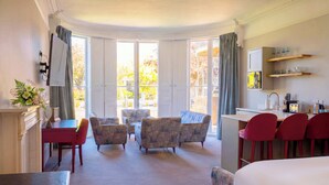 A hotel room with a large bed, a dining area with chairs, a small table, a sofa, a fireplace, and a view of the outdoors. - Poets 24 Apartments (Ely)