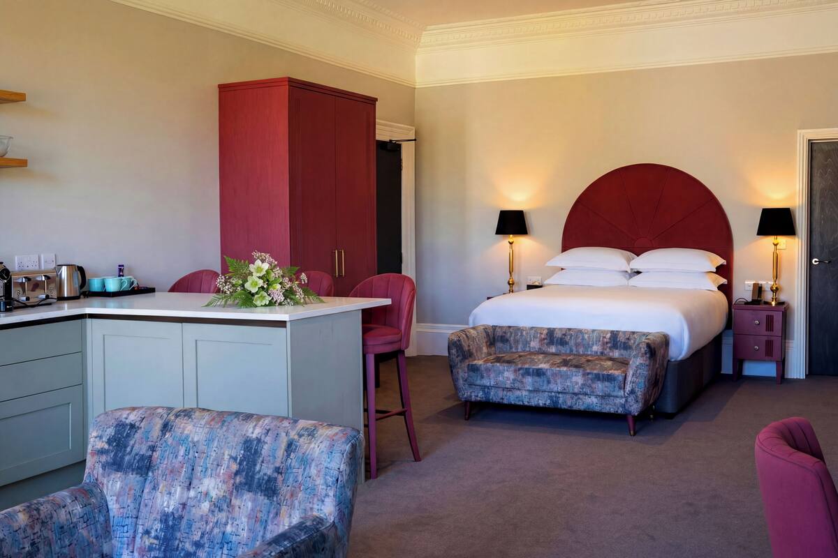 A hotel room with a bed, a desk, a chair, a wardrobe, and a nightstand with lamps.