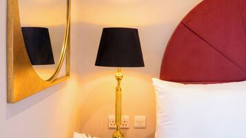 Habitación de hotel con cama, mesita de noche con lámpara, espejo y cómoda roja.