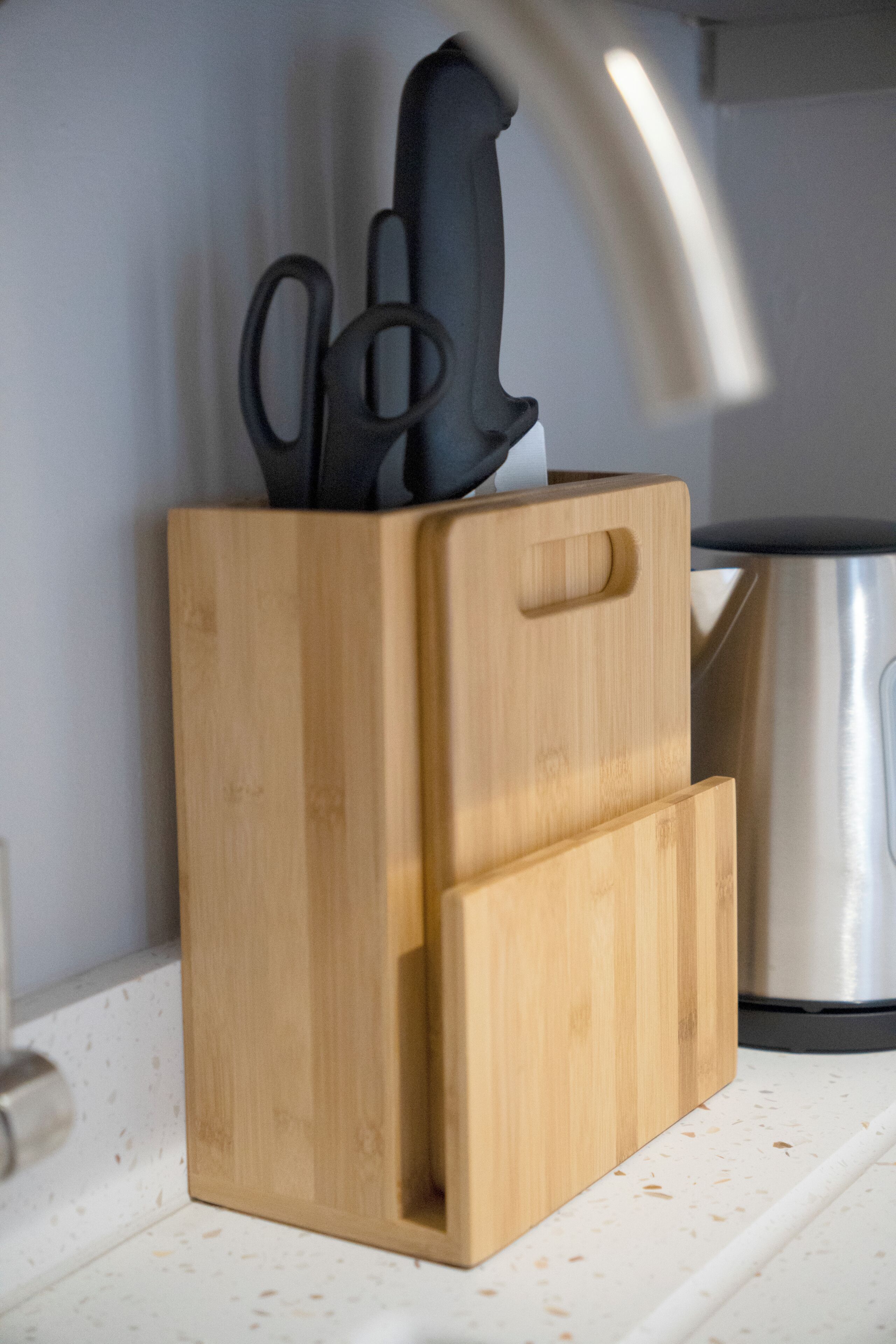 A wooden kitchen utensil block with a knife and scissors on top, a stainless steel pot, and a white countertop.