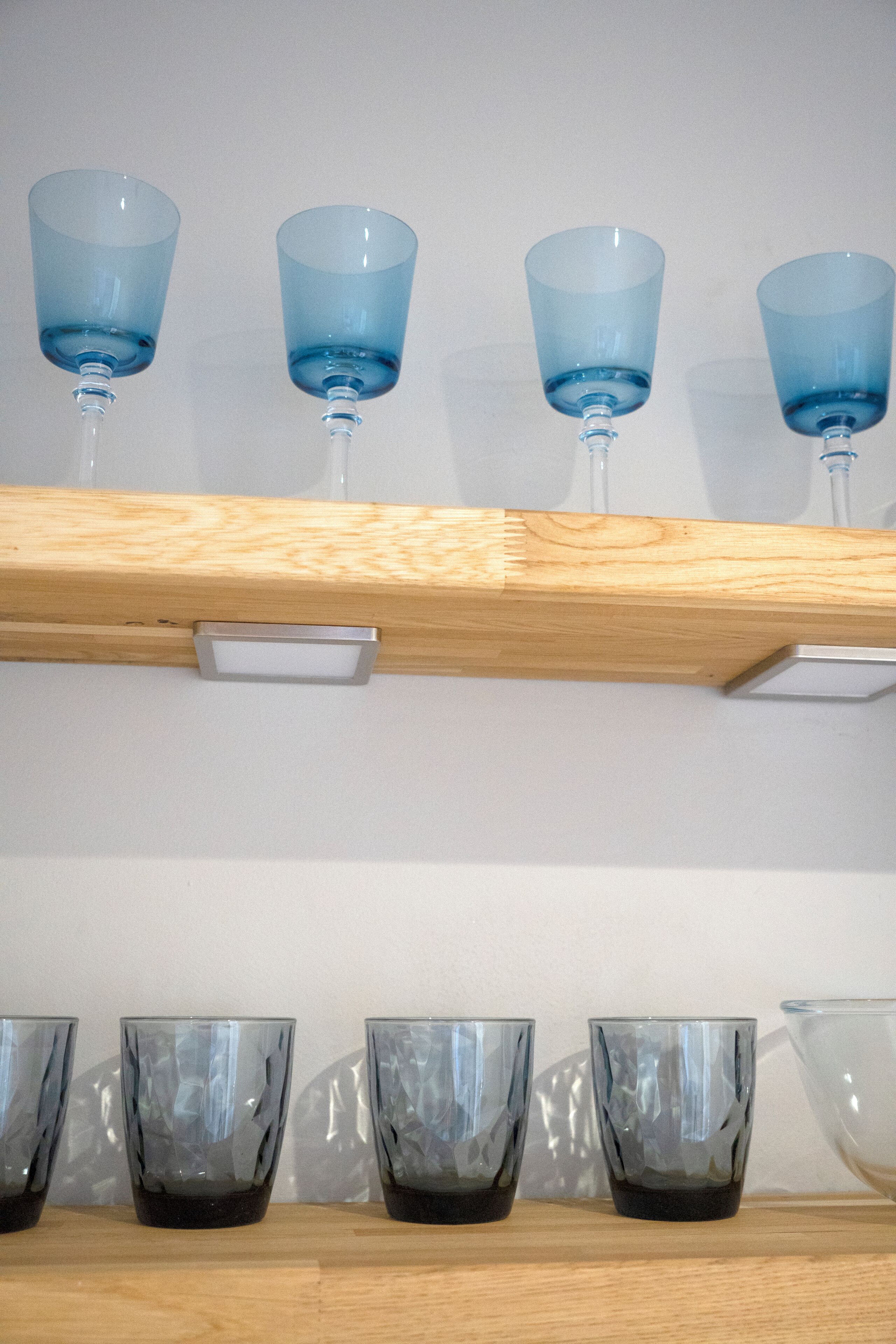 A wooden shelf with blue and clear glassware.