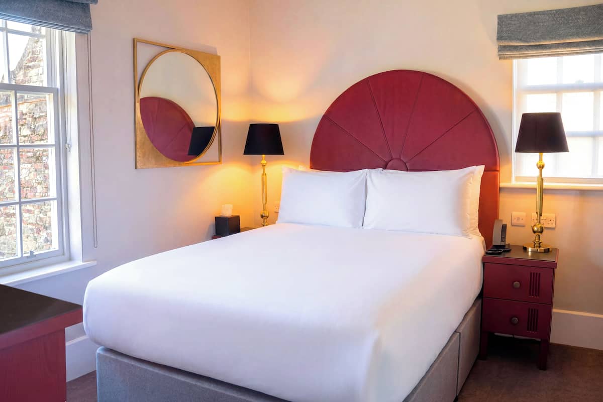 A hotel room with a large bed, bedside lamps, a nightstand, and a window with a view.