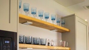 A kitchen with a built-in coffee maker, a sink, and a wooden shelf with blue glasses. - Poets 24 Apartments (Ely)
