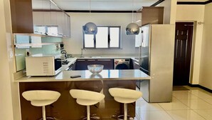 Une cuisine moderne dotée d’un îlot central, de trois tabourets de bar, d’un lave-linge et d’un réfrigérateur.