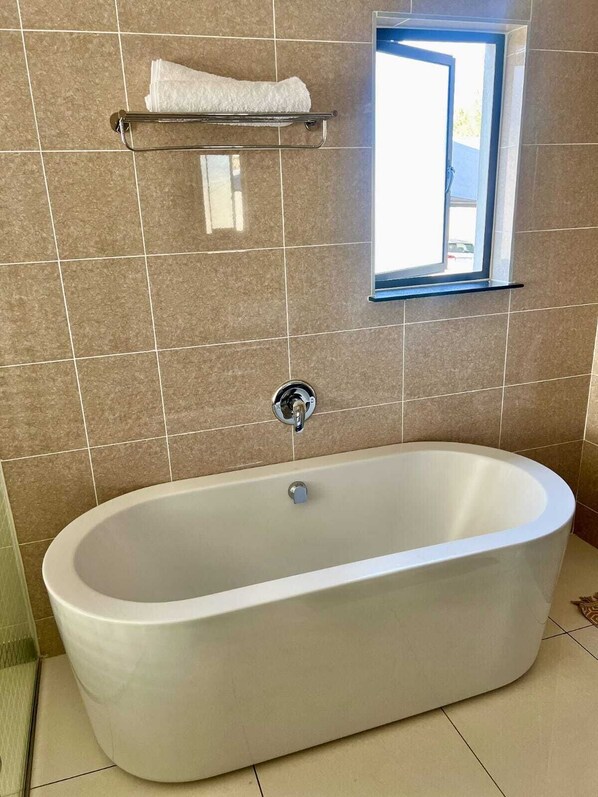 A modern bathroom with a freestanding bathtub, a towel rack, and a window.