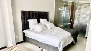 Une chambre moderne avec un grand lit, une douche en verre et un petit coin salon.