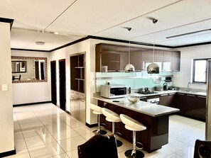 A modern kitchen with a central island, bar stools, and a dining area.