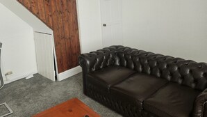 Un sofà de cuir marró fosc amb respatller alt en una habitació amb un panell de paret de fusta i una porta blanca.