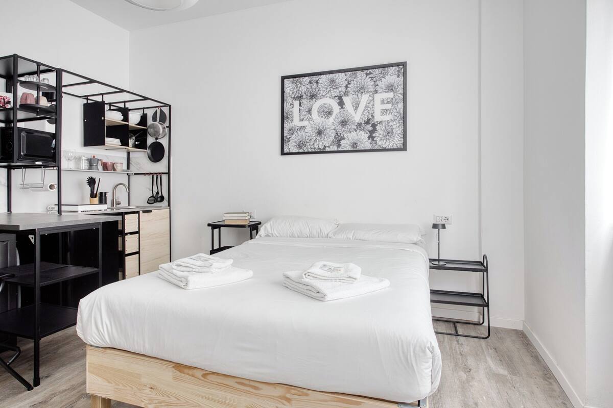 A modern bedroom with a bed, a desk, and a shelving unit.