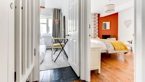 Une pièce comprenant un lit, un bureau et une chaise. Il y a une fenêtre et une porte qui donne sur une autre pièce.
