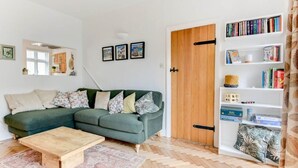 Un salon avec un canapé vert, une table basse en bois et une bibliothèque remplie de livres.