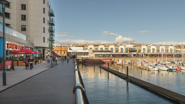 Une promenade en bord de mer avec un port de plaisance, des immeubles dotés de balcons et un restaurant Five Guys.