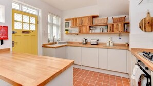Une cuisine avec un plan de travail en bois, des placards blancs, une porte jaune et un sol carrelé.