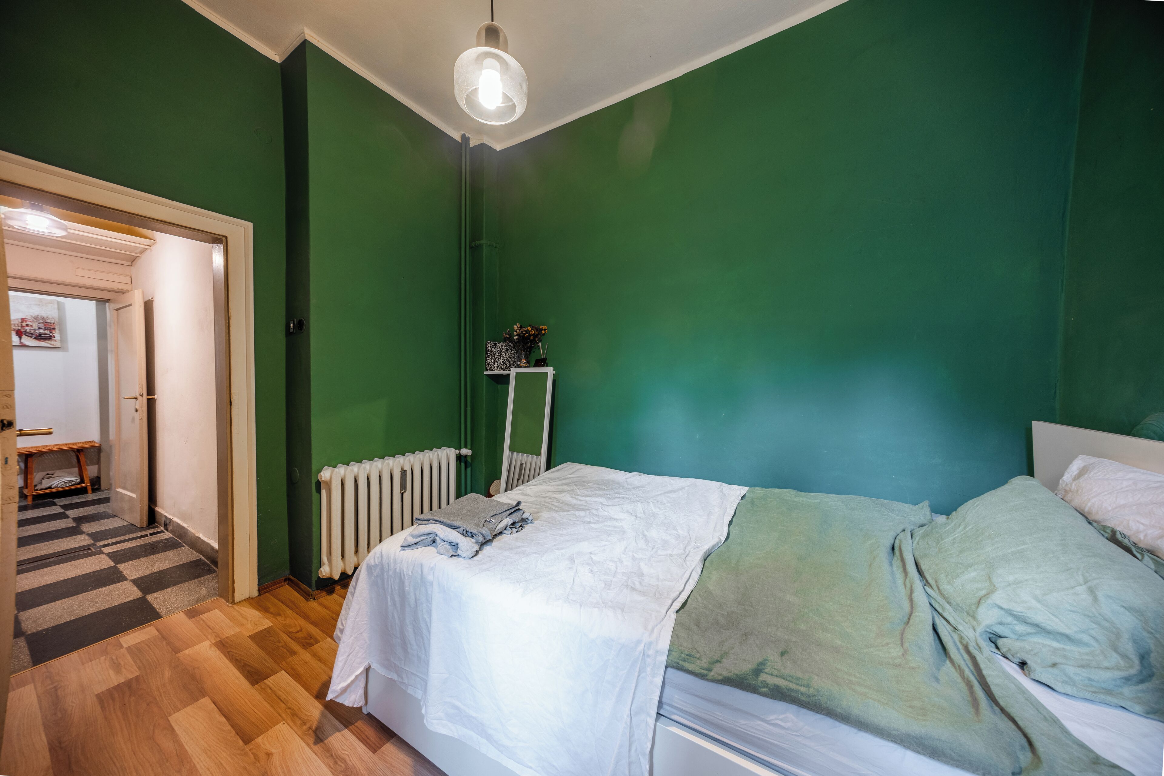 Un dormitorio con una cama, un radiador, un espejo y una puerta que da a otra habitación.