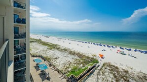 A beach view from a balcony with beach chairs and umbrellas, a clear sky, and a calm sea. - Phoenix X 809 3 Bedroom Condo (Orange Beach)