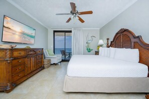 Hotelkamer met een groot bed, plafondventilator, houten dressoir, stoel en balkon met uitzicht.