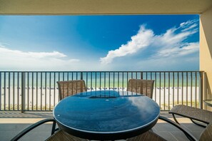 Een balkon met uitzicht op het strand, een ronde tafel en twee stoelen.