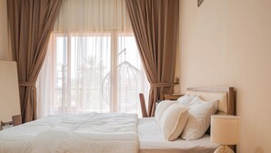 Habitación de hotel con cama, lámpara de noche y vistas a un edificio a través de cortinas traslúcidas.