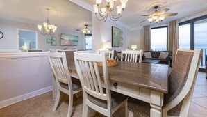 A dining area with a wooden table and white chairs, a chandelier, and a ceiling fan.