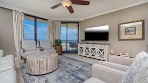 Ein Wohnzimmer mit Deckenventilator, einem Flachbildfernseher, einem runden Couchtisch und Meerblick durch große Fenster.