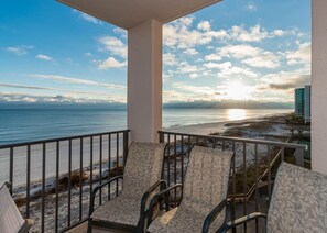 A balcony with three chairs facing a beach and ocean view.