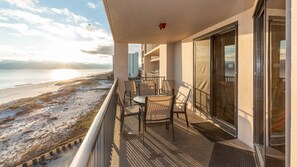 Un balcón con vistas a la playa y al océano, con una mesa y sillas.