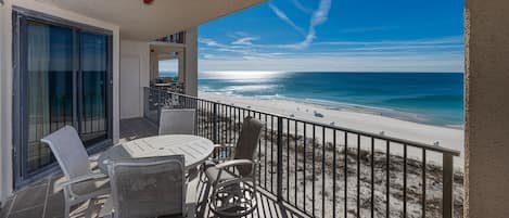 A balcony with a view of the beach, a table with chairs, and a railing.
