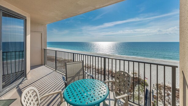 A balcony with a view of the ocean, a table, and two chairs.