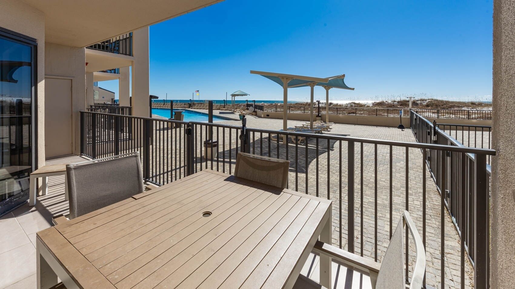 Une terrasse en bois avec une table et des chaises, donnant sur une piscine et une plage.