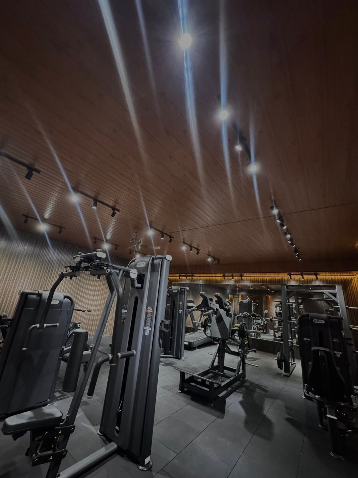 A gym with various exercise machines, wooden ceiling, and multiple ceiling lights.