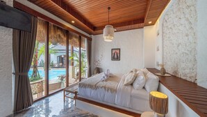 A bedroom with a wooden ceiling, a large bed, a nightstand, a lamp, and a view of a swimming pool. - Casa Maddu (Sebatu)