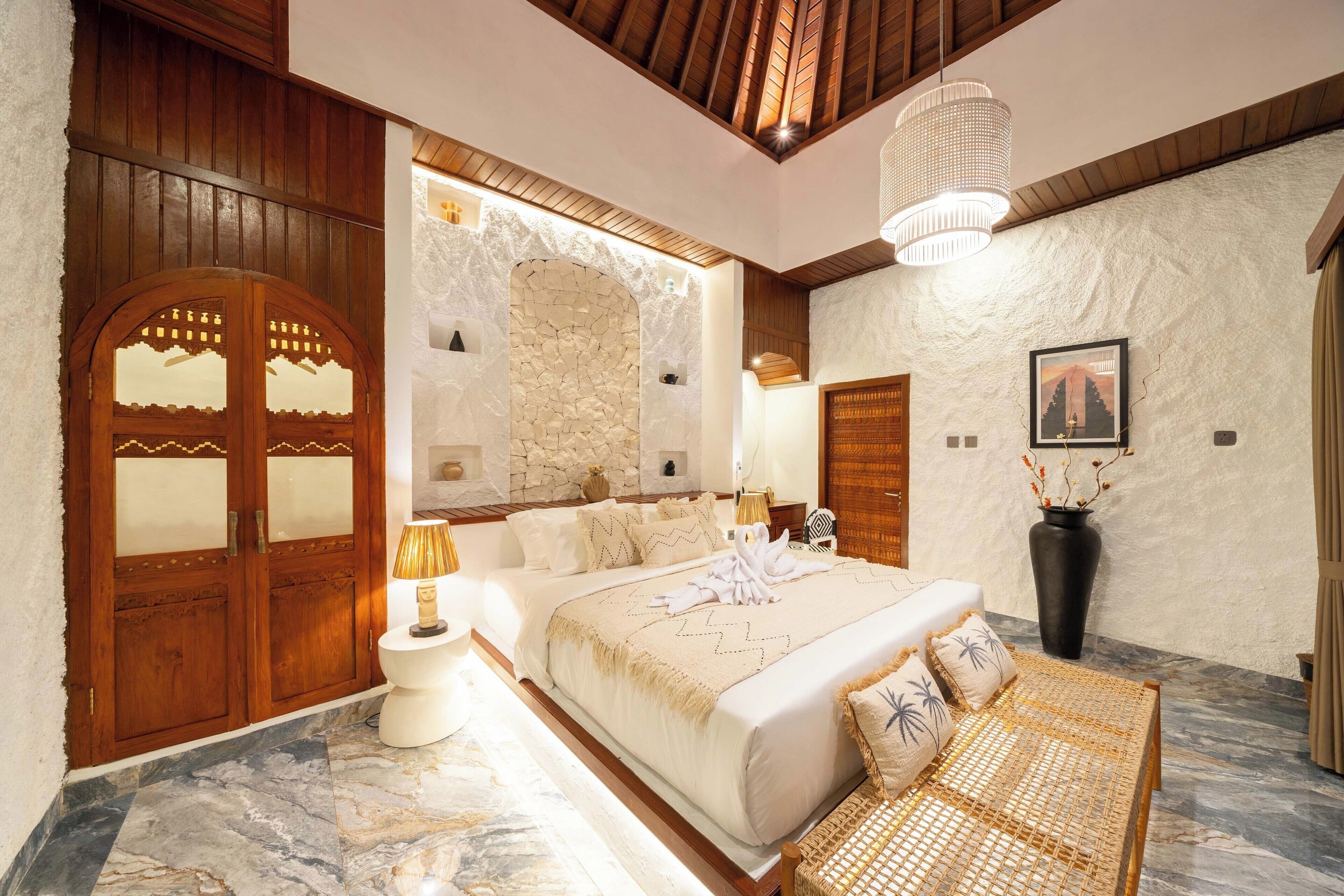 Un dormitorio amplio con una cama grande, puertas de madera, paredes de piedra y suelo de mármol.