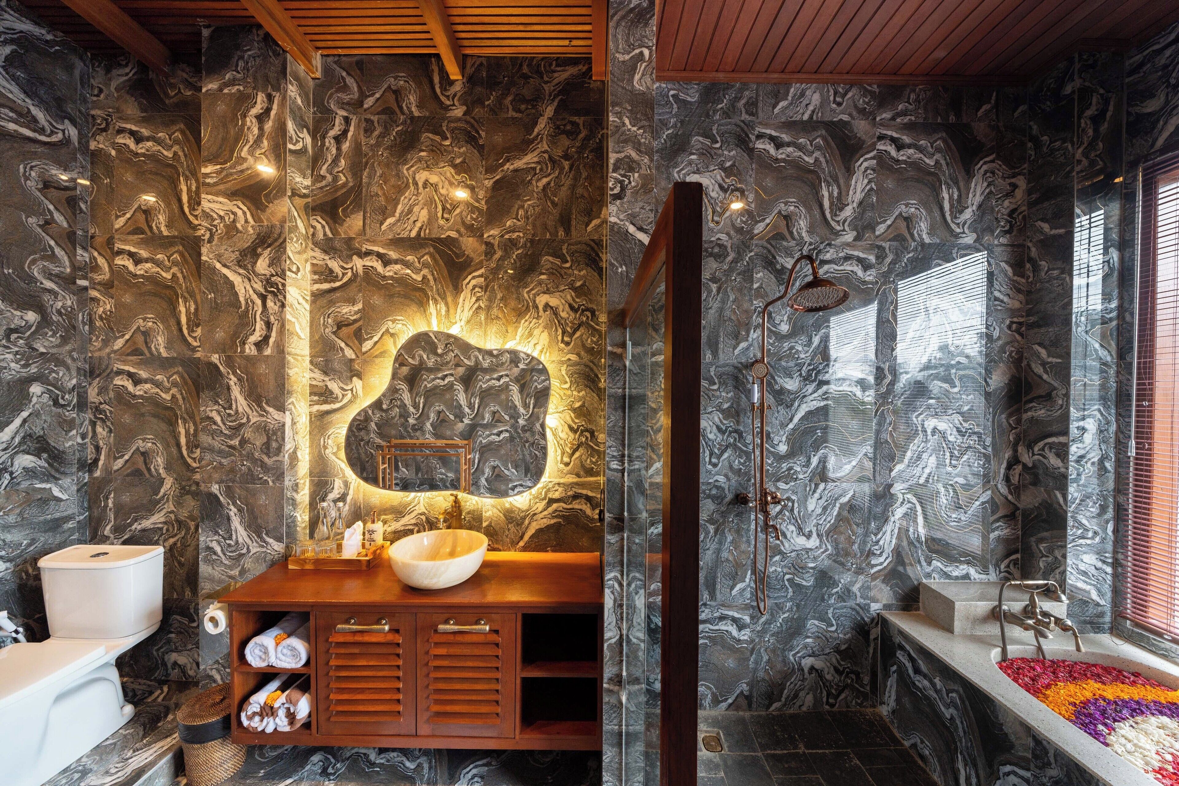 A bathroom with marble walls, a wooden vanity, a large mirror, and a bathtub with a colorful mosaic.