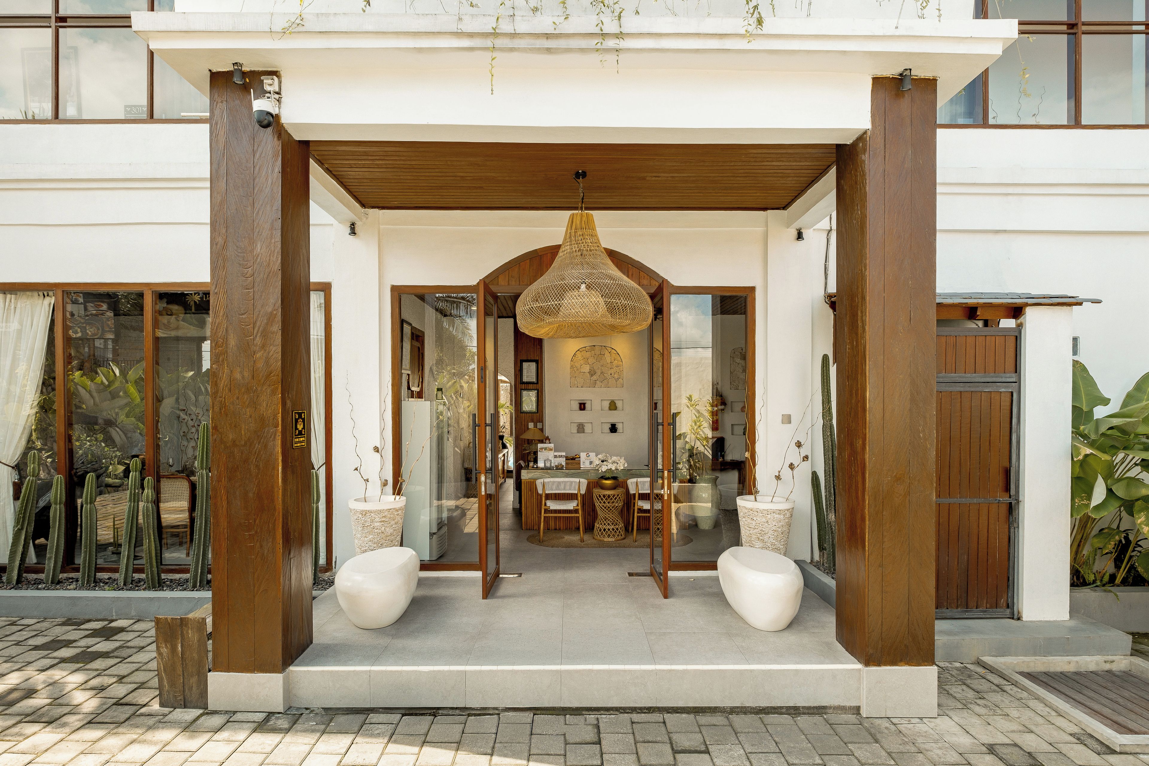 A modern building entrance with a covered porch, a hanging light fixture, and a view into the interior.