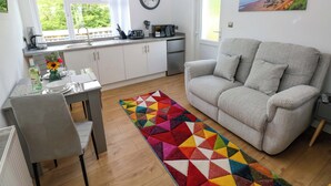 Una cocina moderna con armarios blancos, un comedor con una mesa dispuesta para dos personas y una alfombra geométrica y colorida.