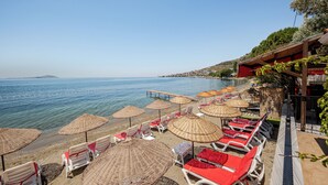 Blick auf einen Strand mit Reihen von Liegestühlen und Reetdachschirmen, ein klares blaues Meer und eine entfernte Insel.