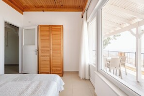 A bedroom with a bed, a wooden wardrobe, and a balcony with chairs.