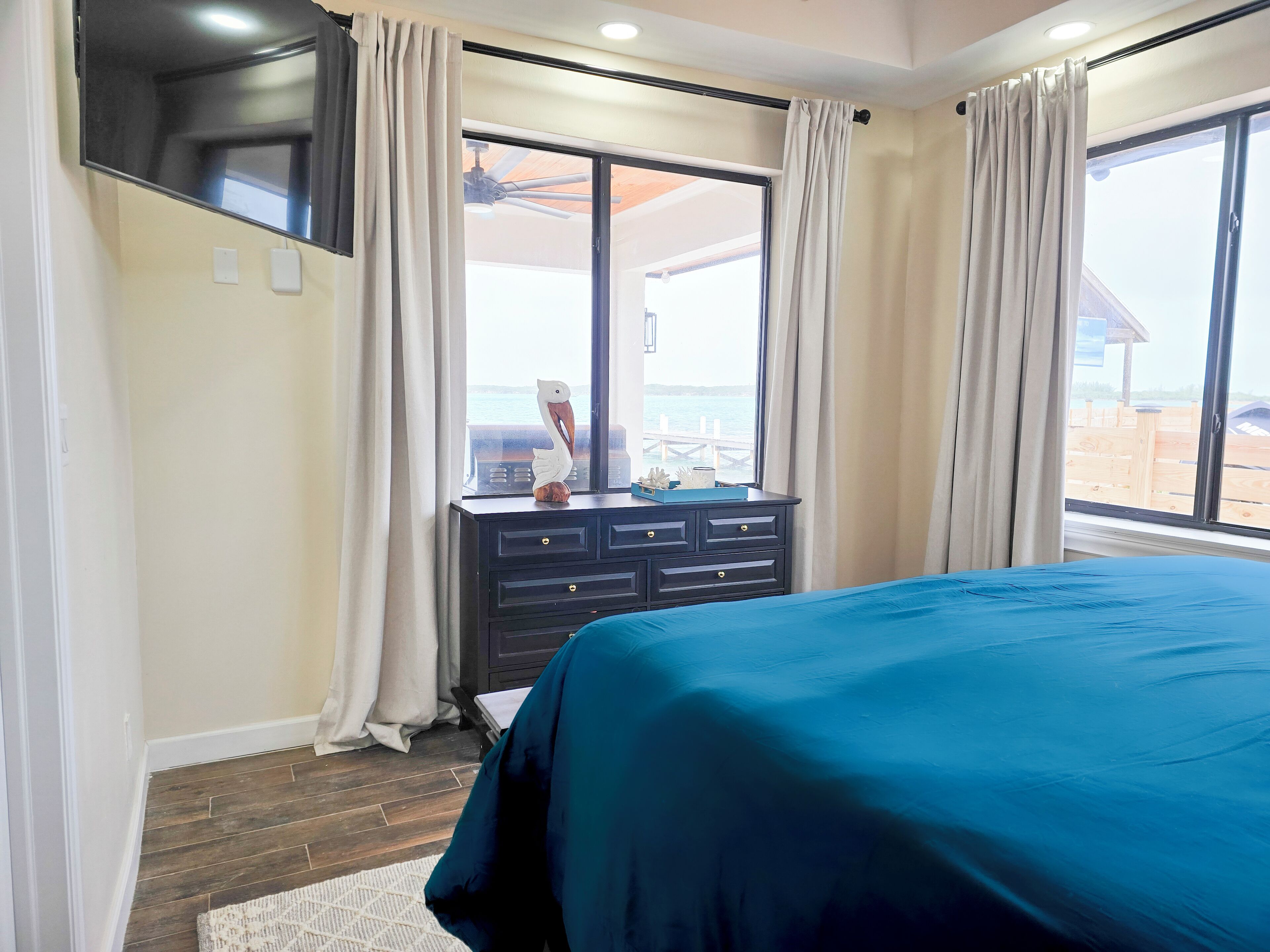A bedroom with a bed, a dresser, and a window with a view of the sea.
