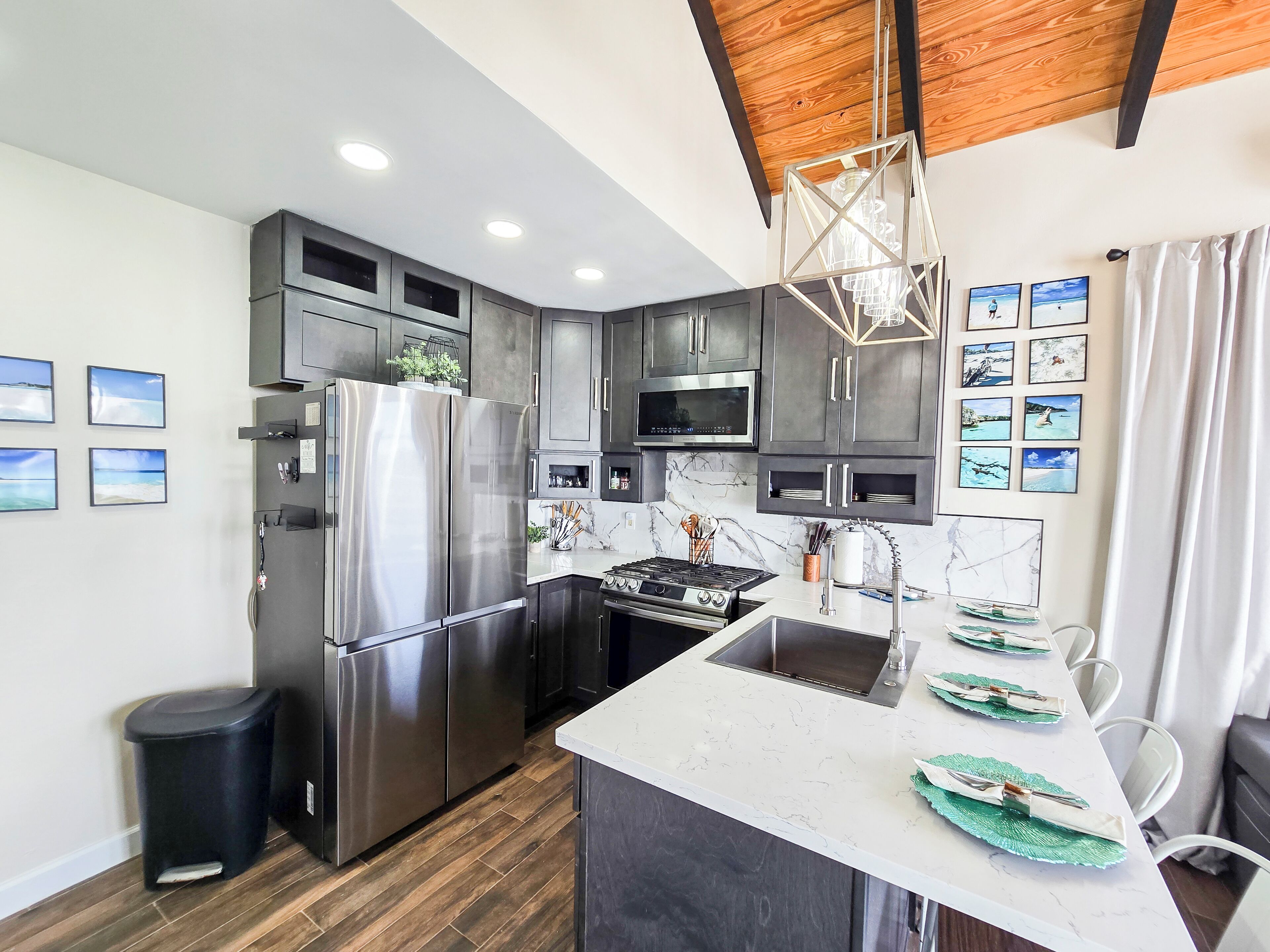 A modern kitchen with stainless steel appliances, a marble countertop, and a wooden ceiling.