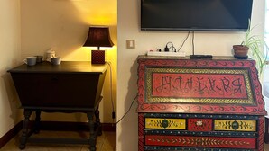 A room with a wooden floor, a dark wooden cabinet with colorful floral patterns, a television mounted on the wall, and a lamp on a table. - Bed and breakfast in Castelfranc, ideal for a cycling stopover in the Lot valley (Castelfranc)