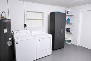 Ein Waschraum mit zwei weißen Waschmaschinen, einem schwarzen Schrank und Regalen mit Reinigungsmitteln.